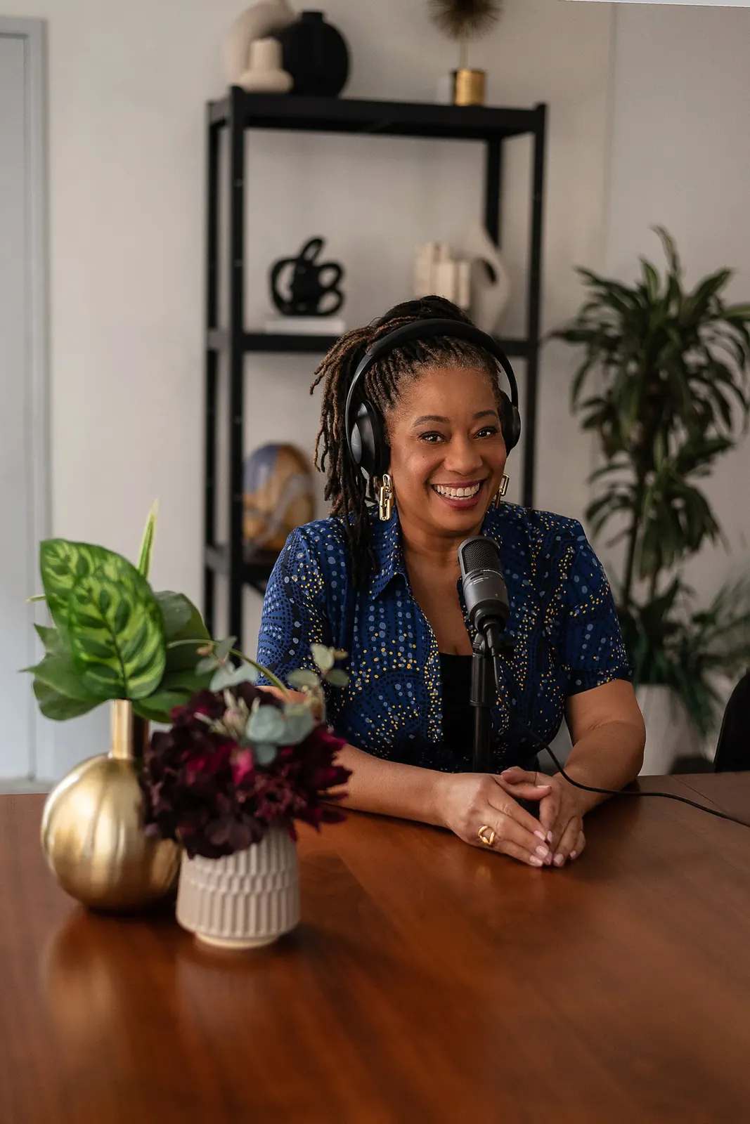 Lisane Basquiat smiling at the microphone with headphones on, flowers and plants in her studio