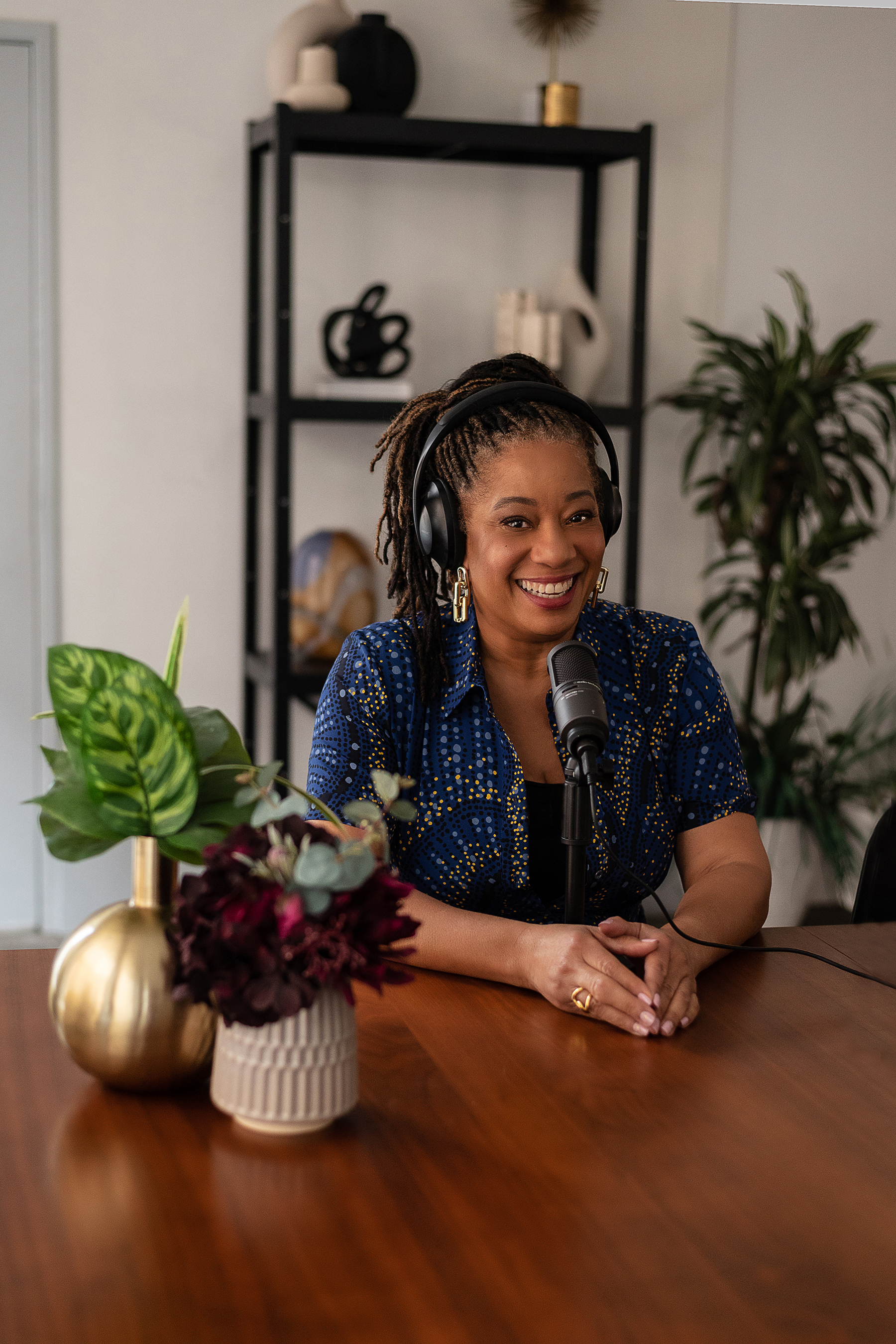 Lisane Basquiat smiling at the microphone with headphones on, flowers and plants in her studio