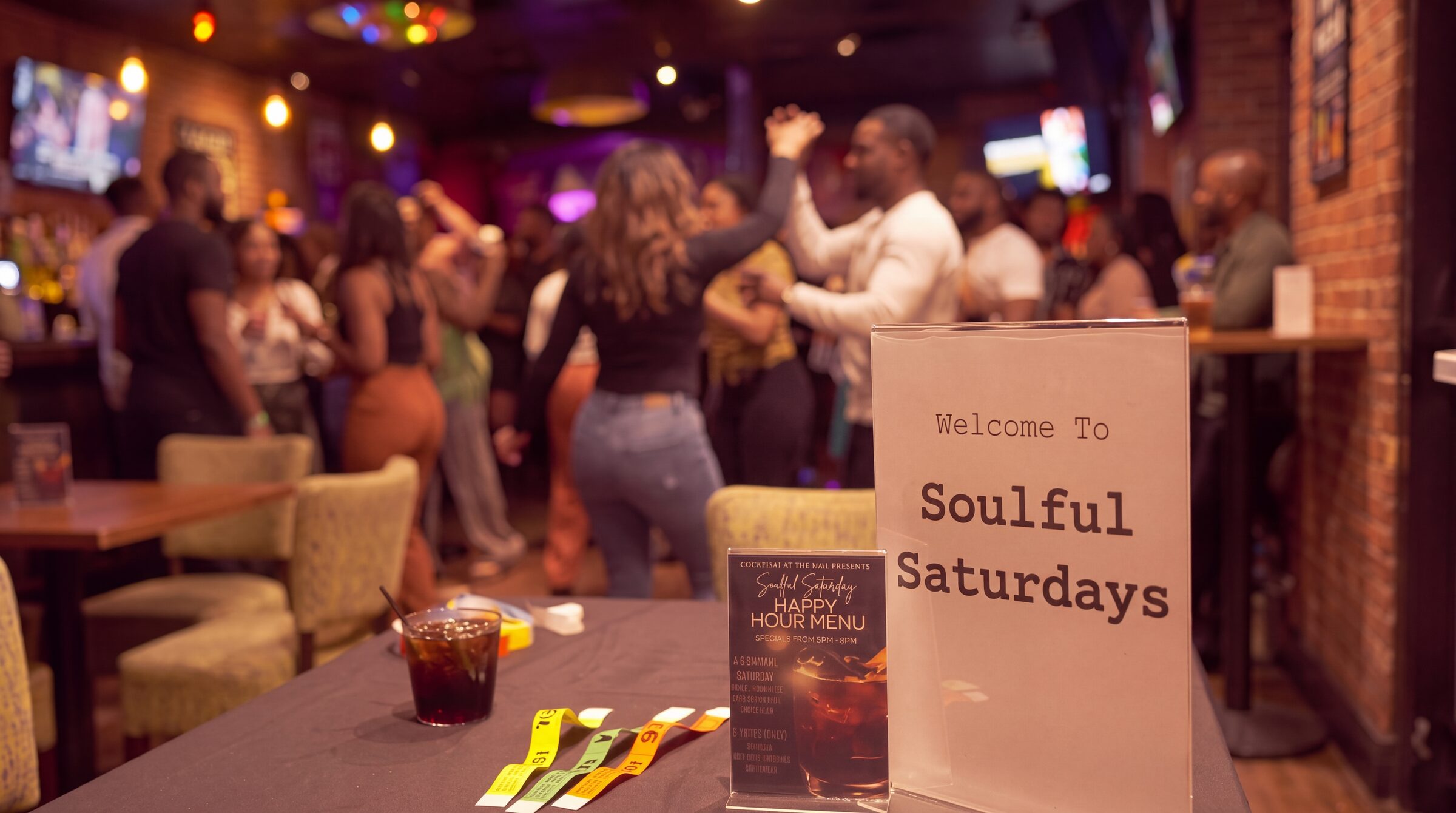 Guests dancing at a Soulful Saturdays gathering, beside a “Welcome to Soulful Saturdays” sign