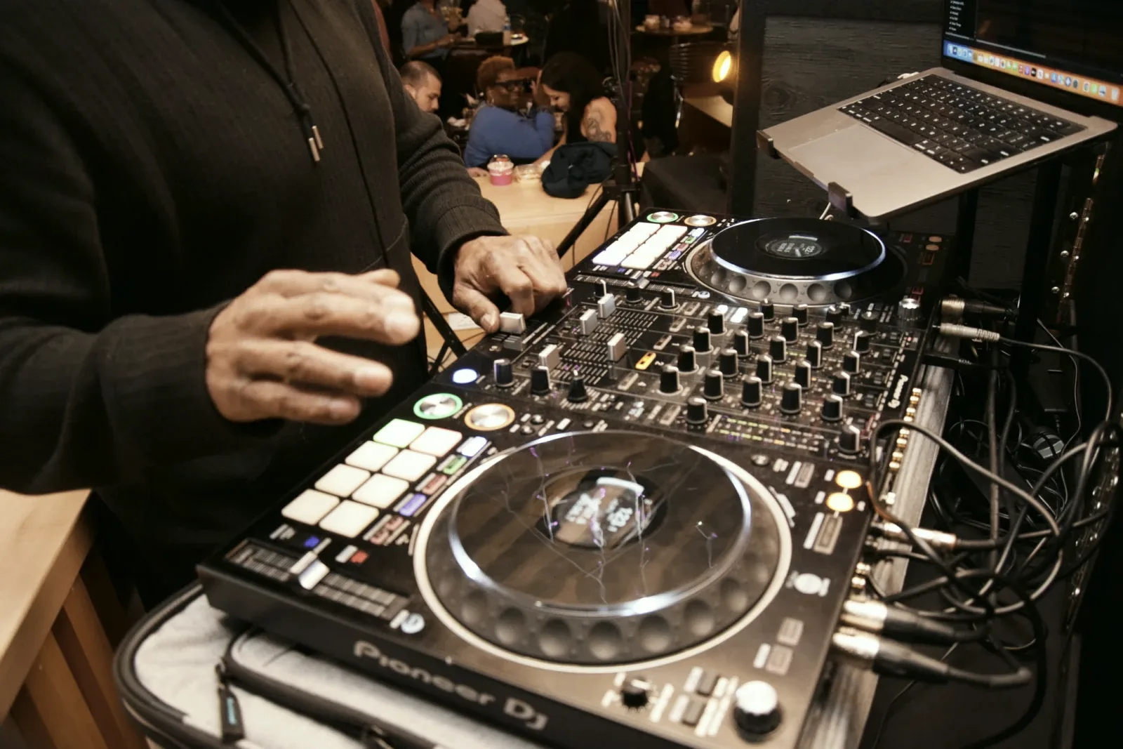 A DJ mixing at a Soulful Saturdays gathering, guests talking around tables behind the decks