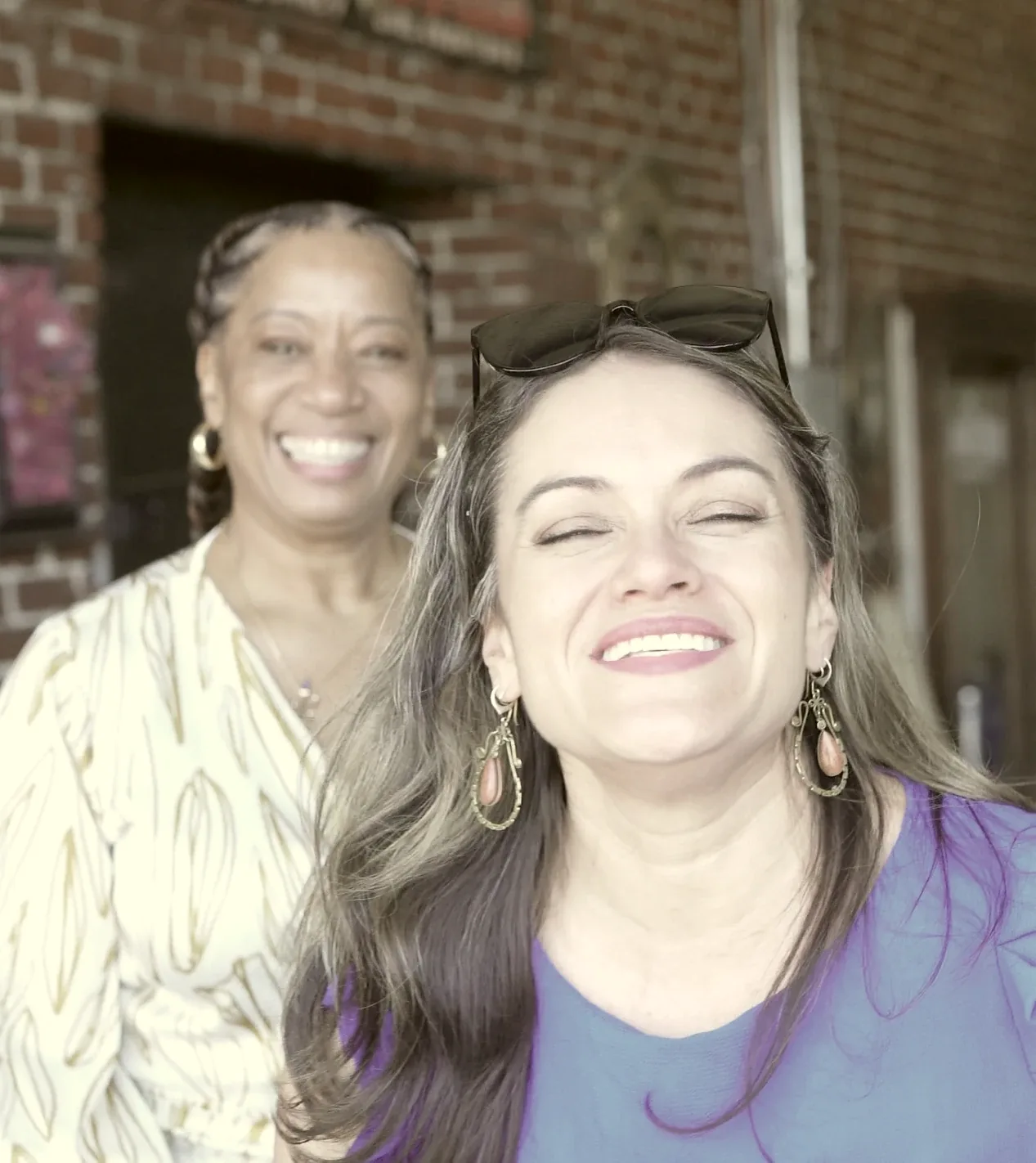 Two women laughing together outside a brick building.